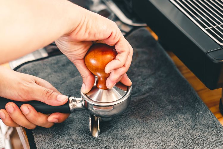 The barista presses ground coffee using a tamper on a wooden