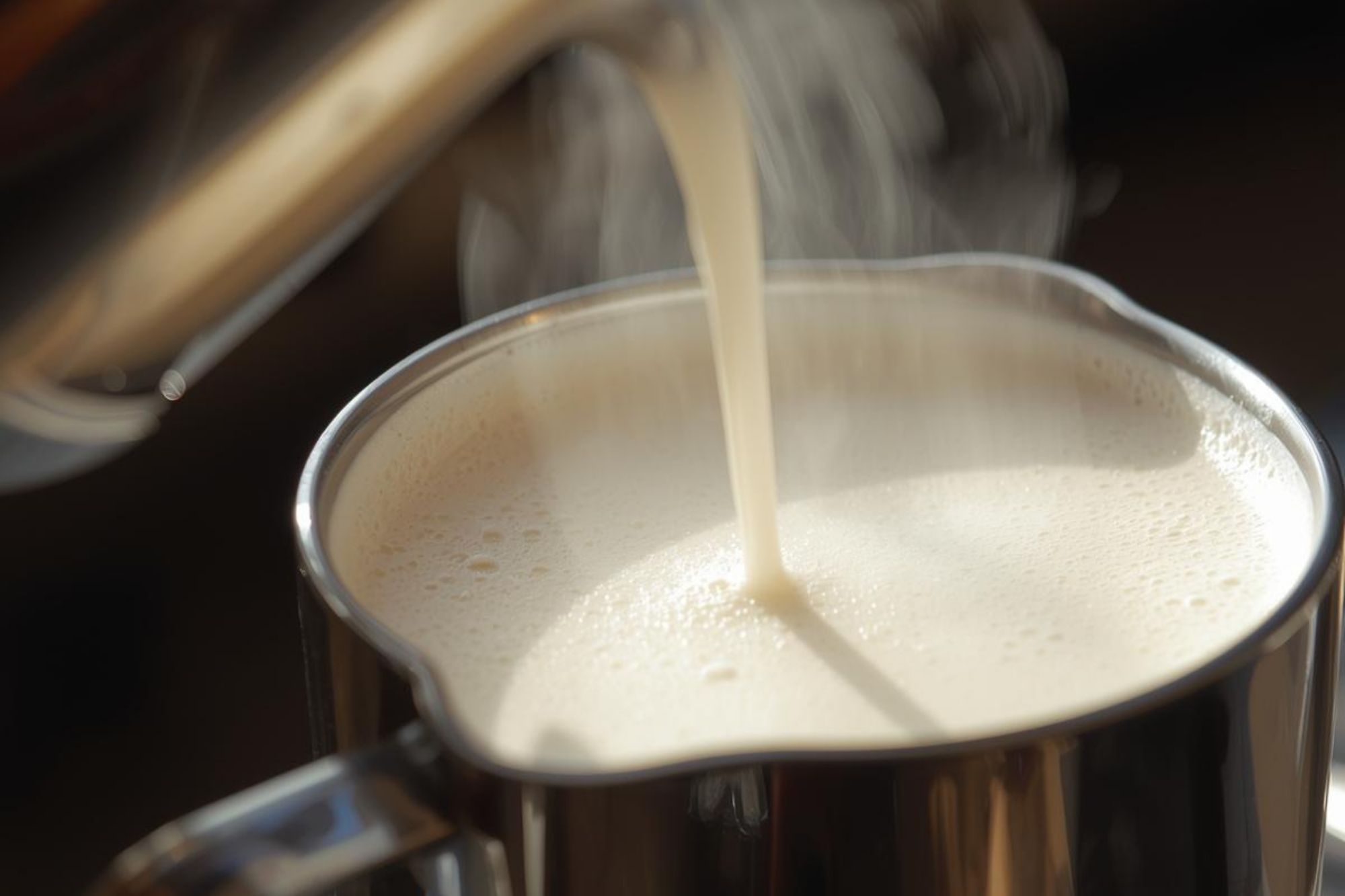 A close-up of a steamed pitcher of oat milk (barista style), showing fine, stable microfoam ready for pouring.