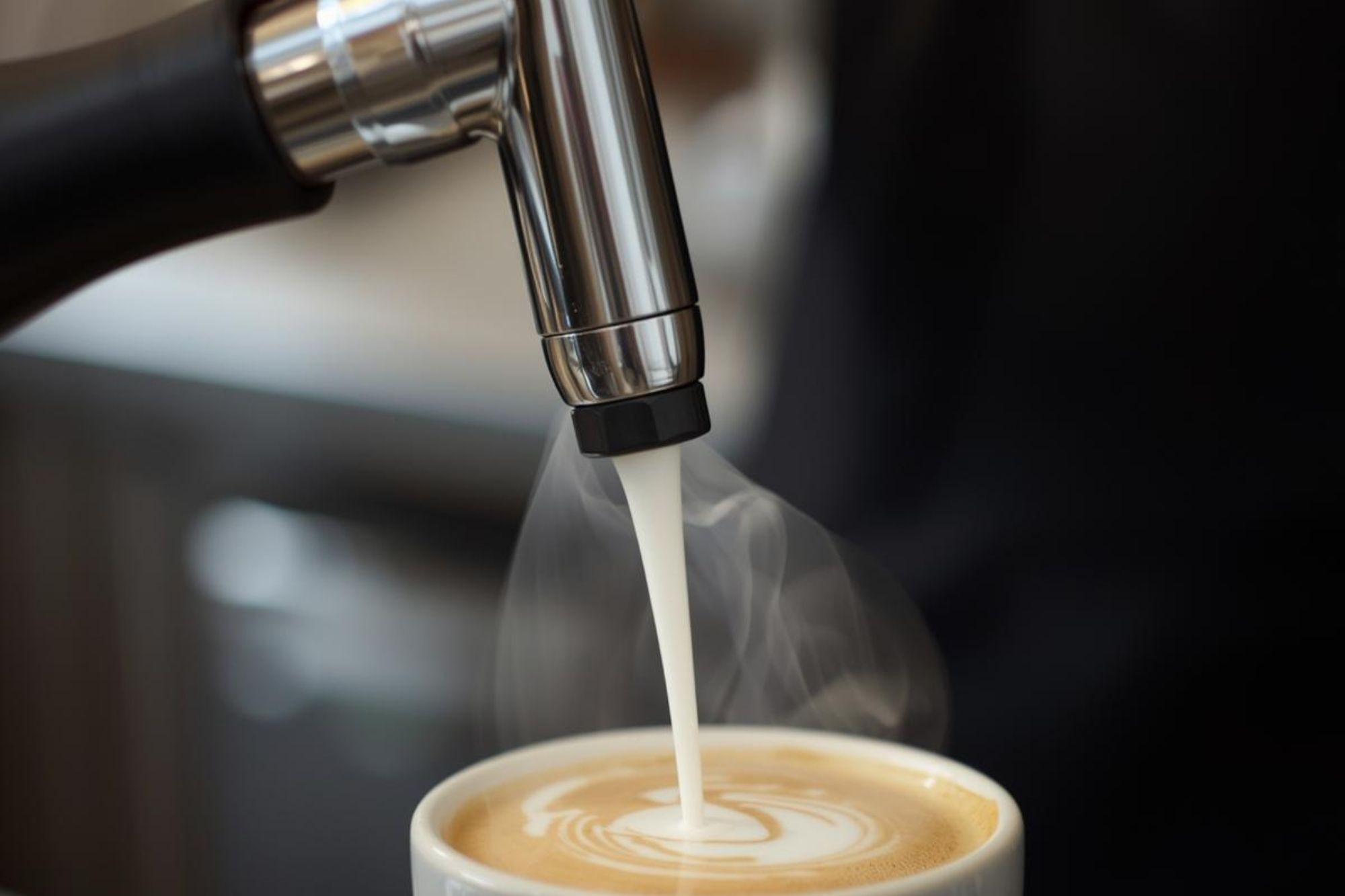 A close-up photo of a barista actively steaming milk with a powerful, commercial steam wand, emphasizing the necessary pressure and speed.