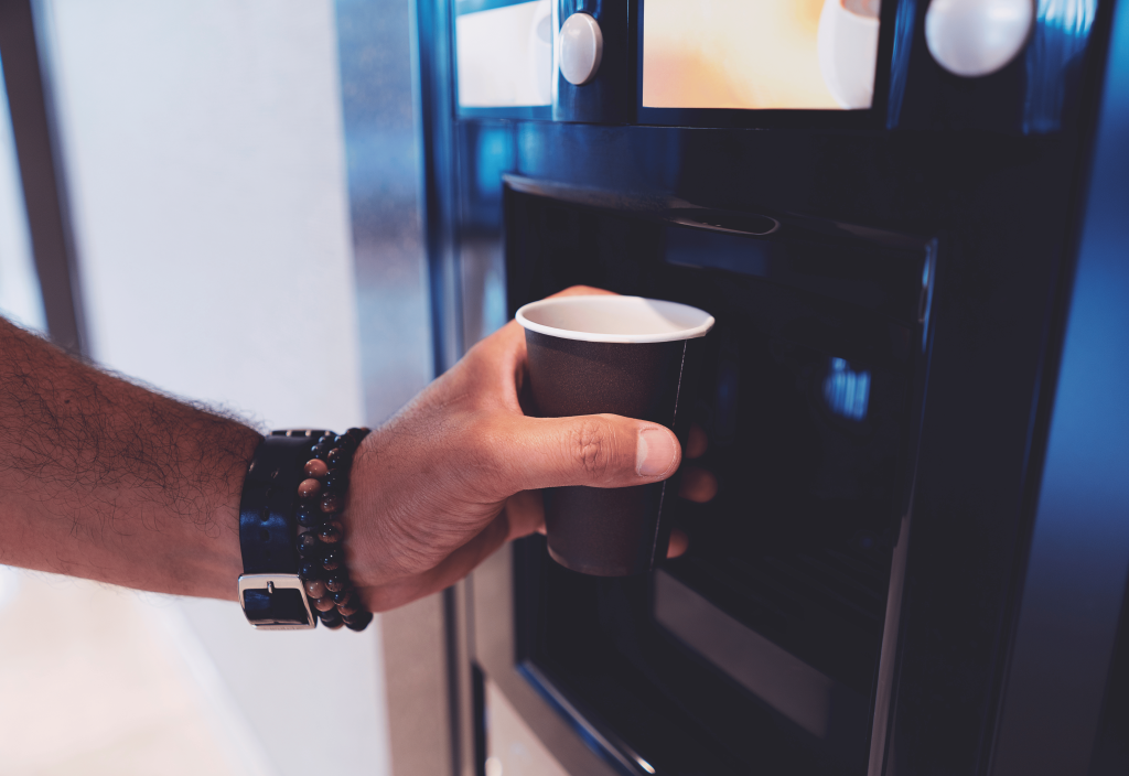 a hand holding a paper cup to a coffee machine waiting for the coffee to pour