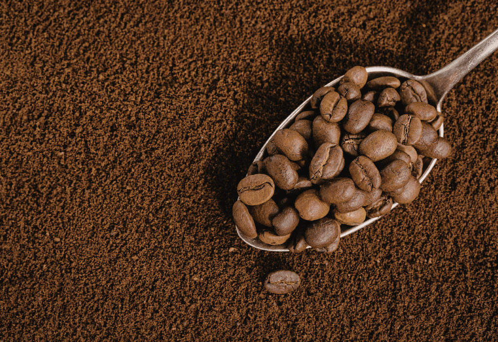 coffee beans in a spoon amid ground coffee background