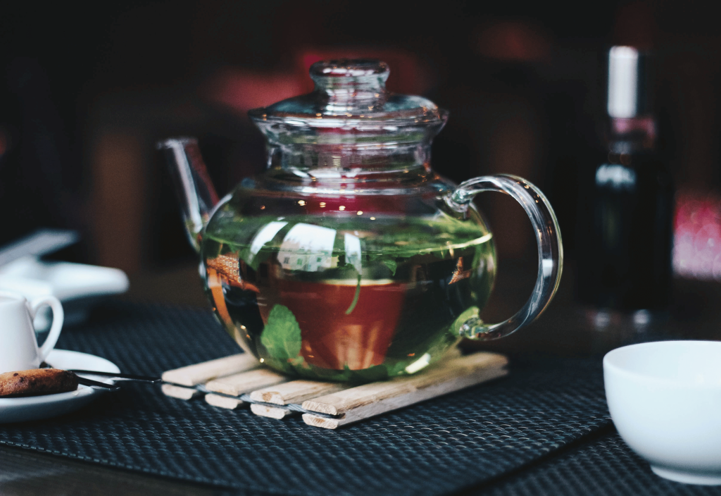 glass teapot half full of red tea and mint leaves